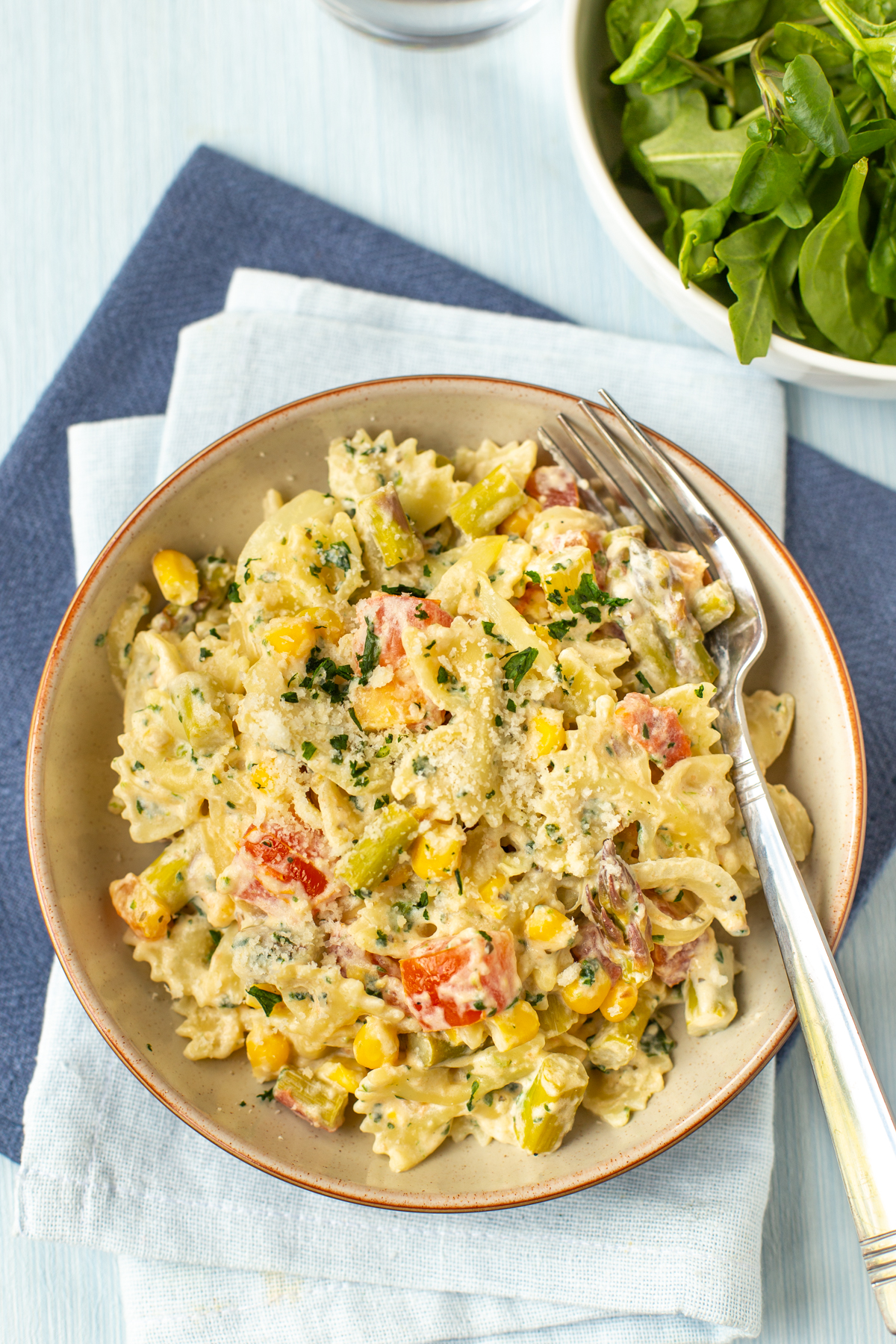 A portion of pasta primavera in a bowl with parmesan and parsley.