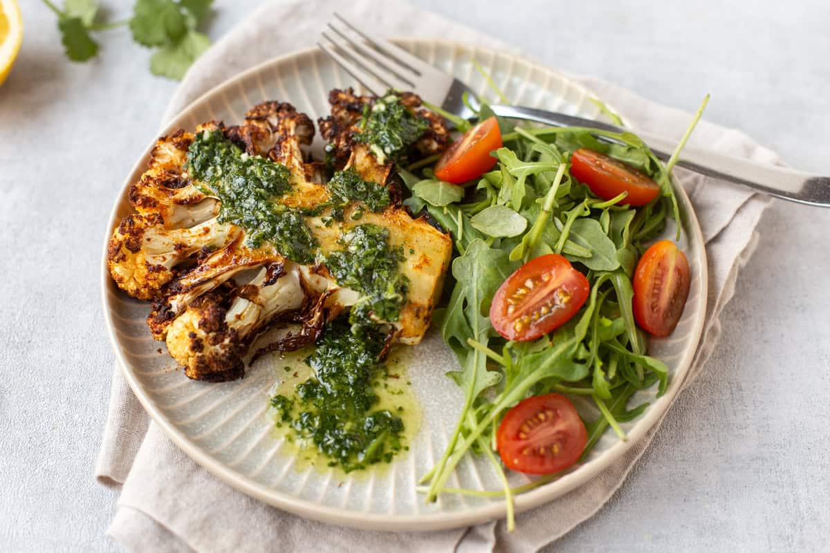 An air fried cauliflower steak on a plate with cilantro dressing and salad.