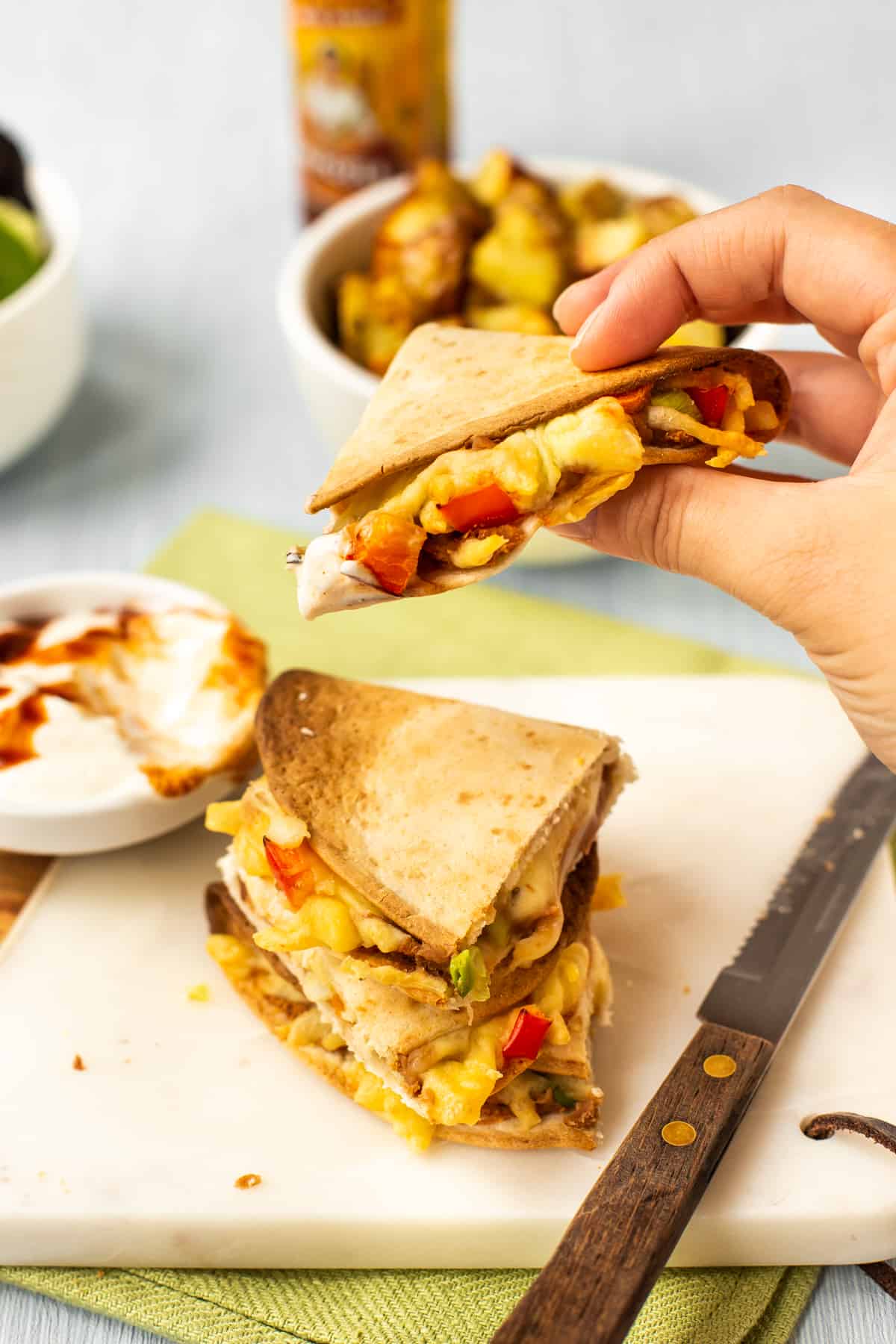 A hand lifting up a piece of cheesy air fried quesadilla.