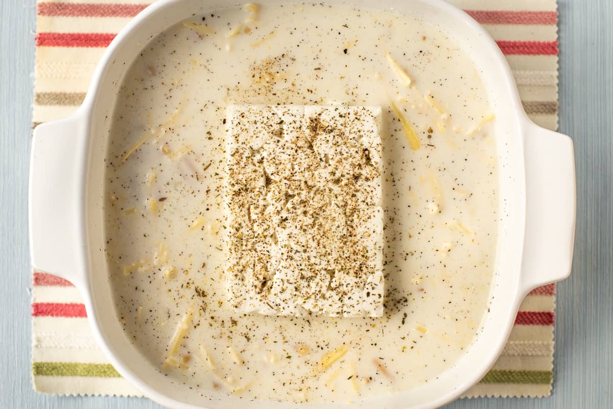 A baking dish with uncooked pasta in milk and a block of feta cheese.