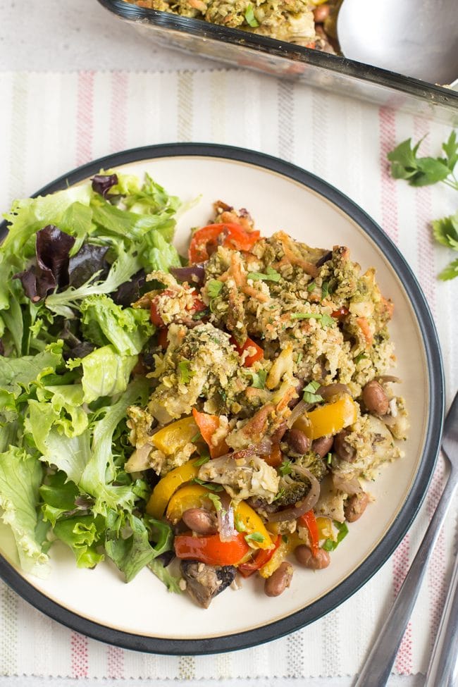Portion of bean and vegetable crumble on a plate with salad, shot from above