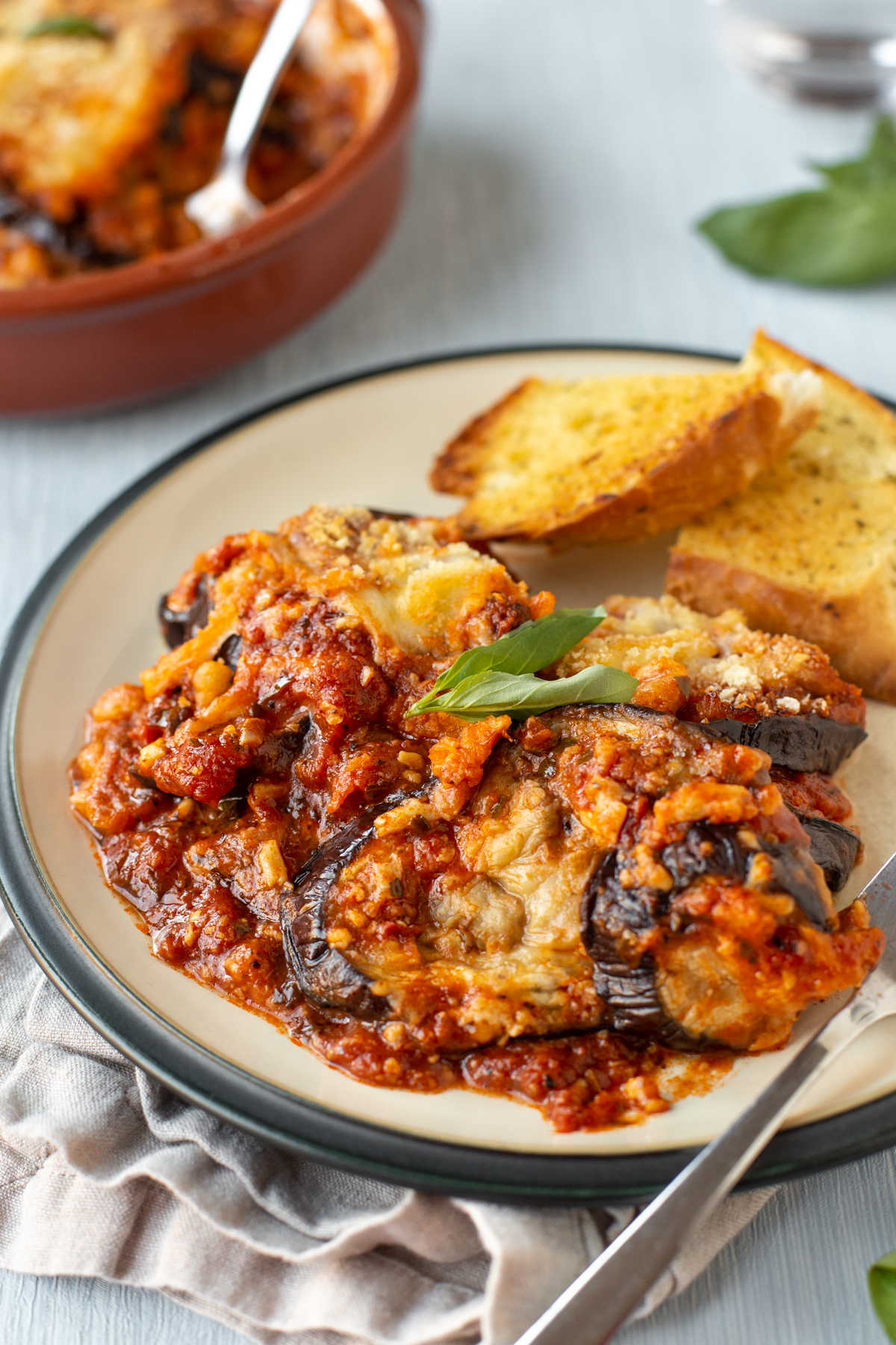 A portion of cheesy eggplant bake on a plate with garlic bread.