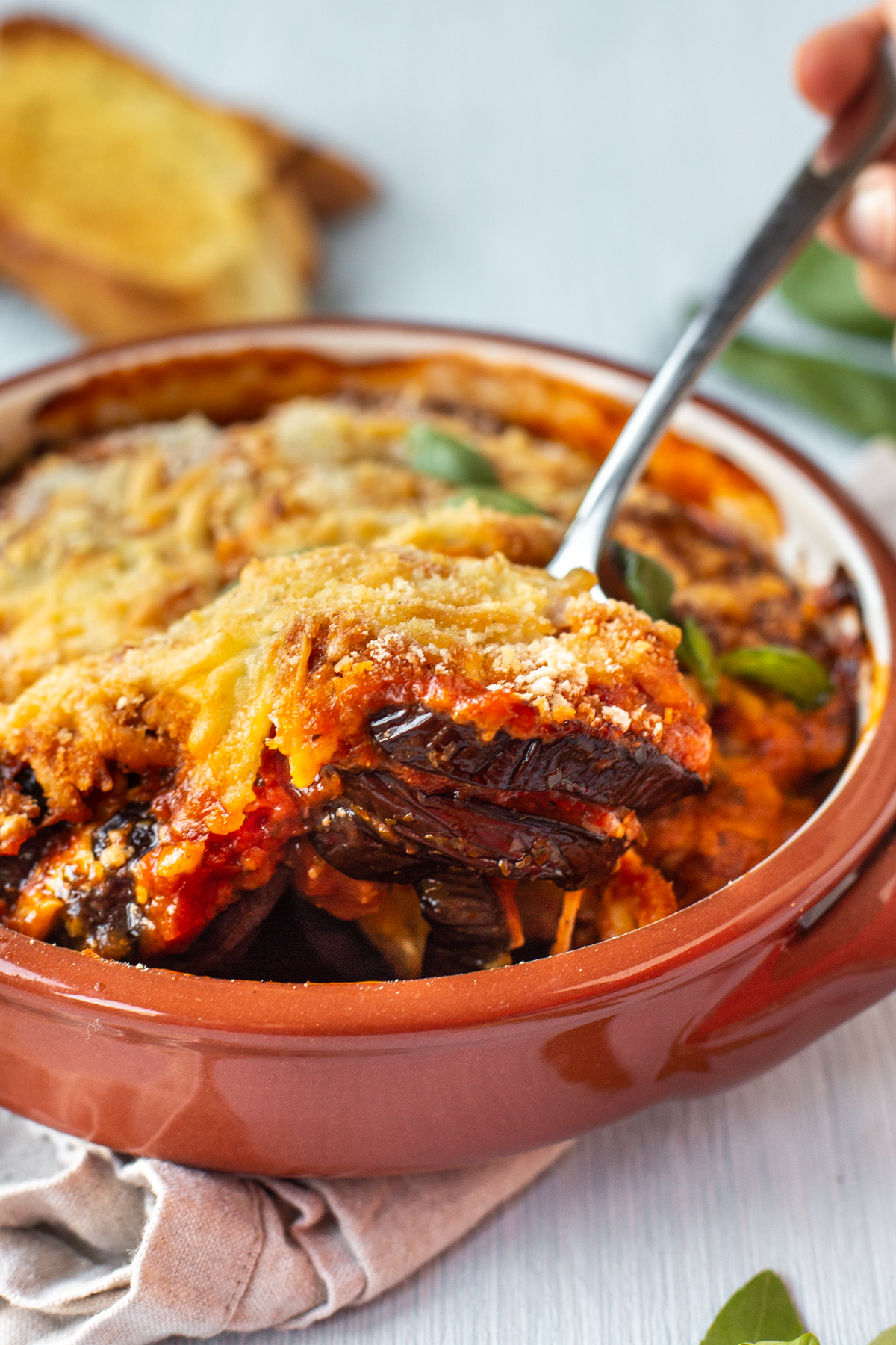 A spoon beginning to scoop some cheesy eggplant bake with tomato sauce.