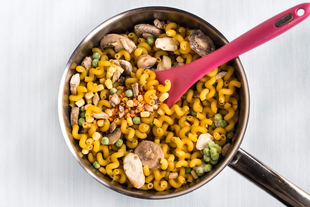 Uncooked pasta, lentils and frozen vegetables in a pan.