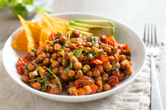 Nacho roasted chickpeas in a bowl with tortilla chips and avocado