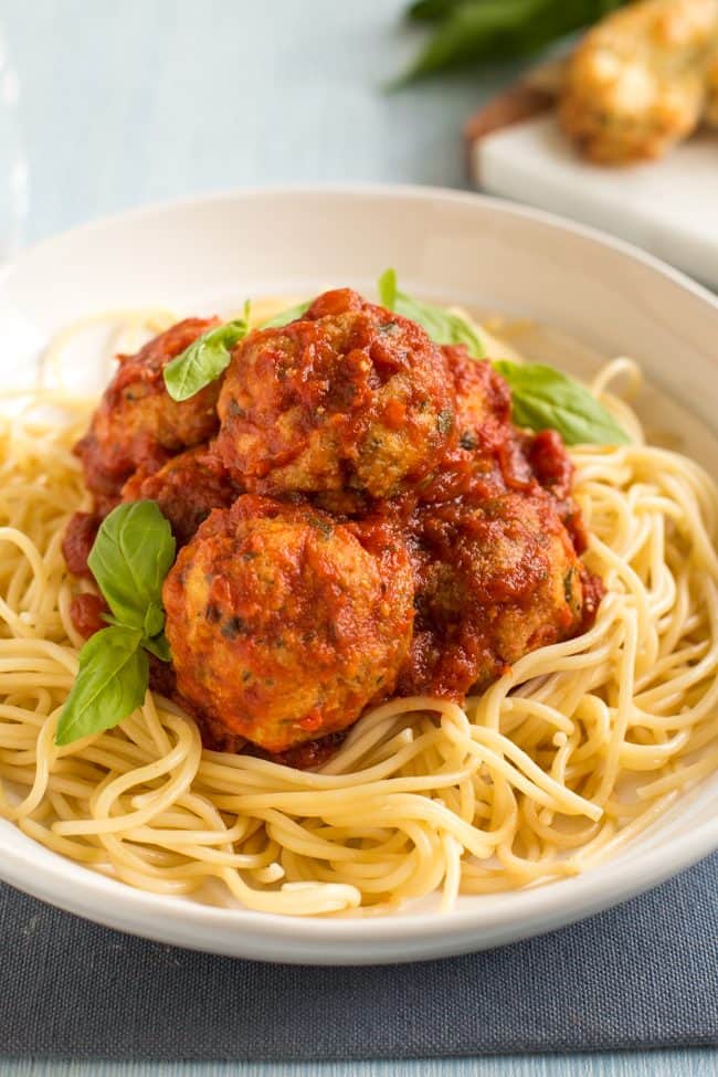 Portion of cheesy tofu meatballs in a bowl with spaghetti and fresh basil