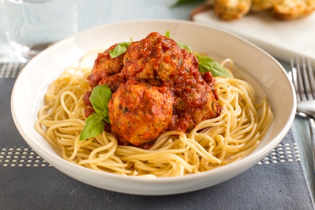 Portion of cheesy tofu meatballs in a bowl with spaghetti and fresh basil