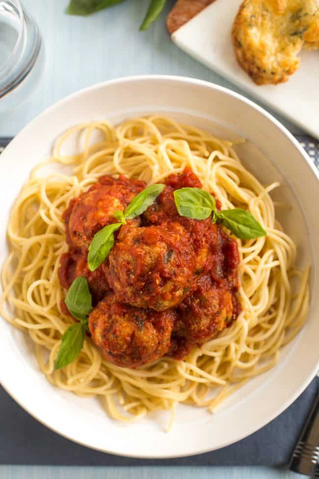Portion of cheesy tofu meatballs in a bowl with spaghetti and fresh basil, shot from above