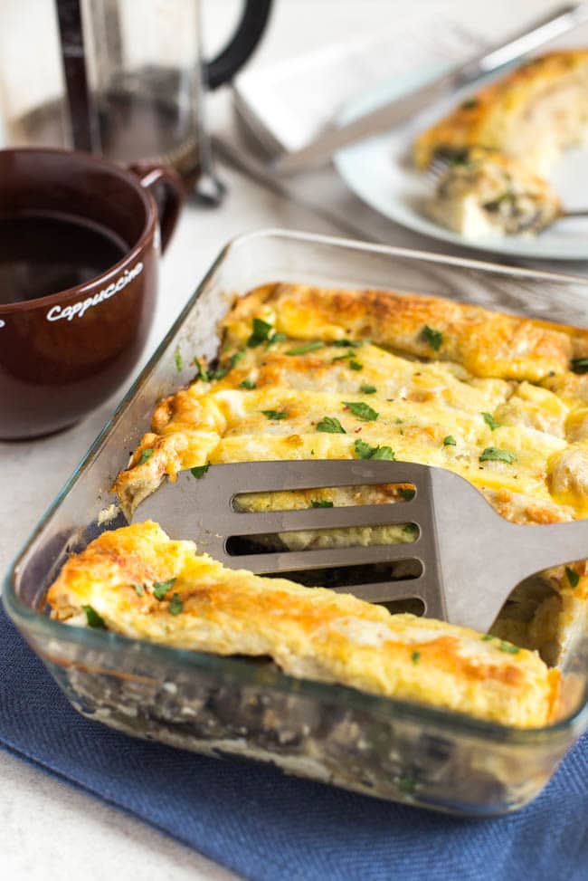 A spatula scooping a rolled tortilla from a pan of cheesy breakfast bake.
