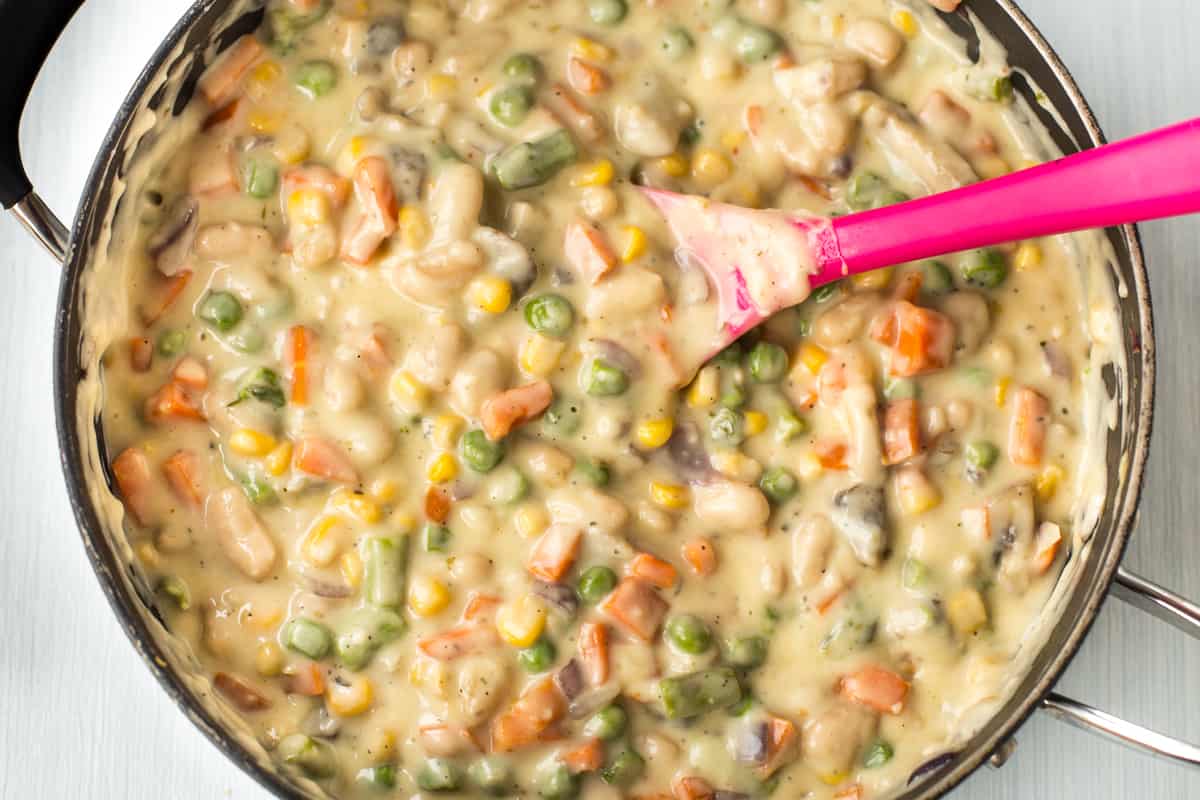 Colourful vegetables coated in a cheesy sauce in a pan.