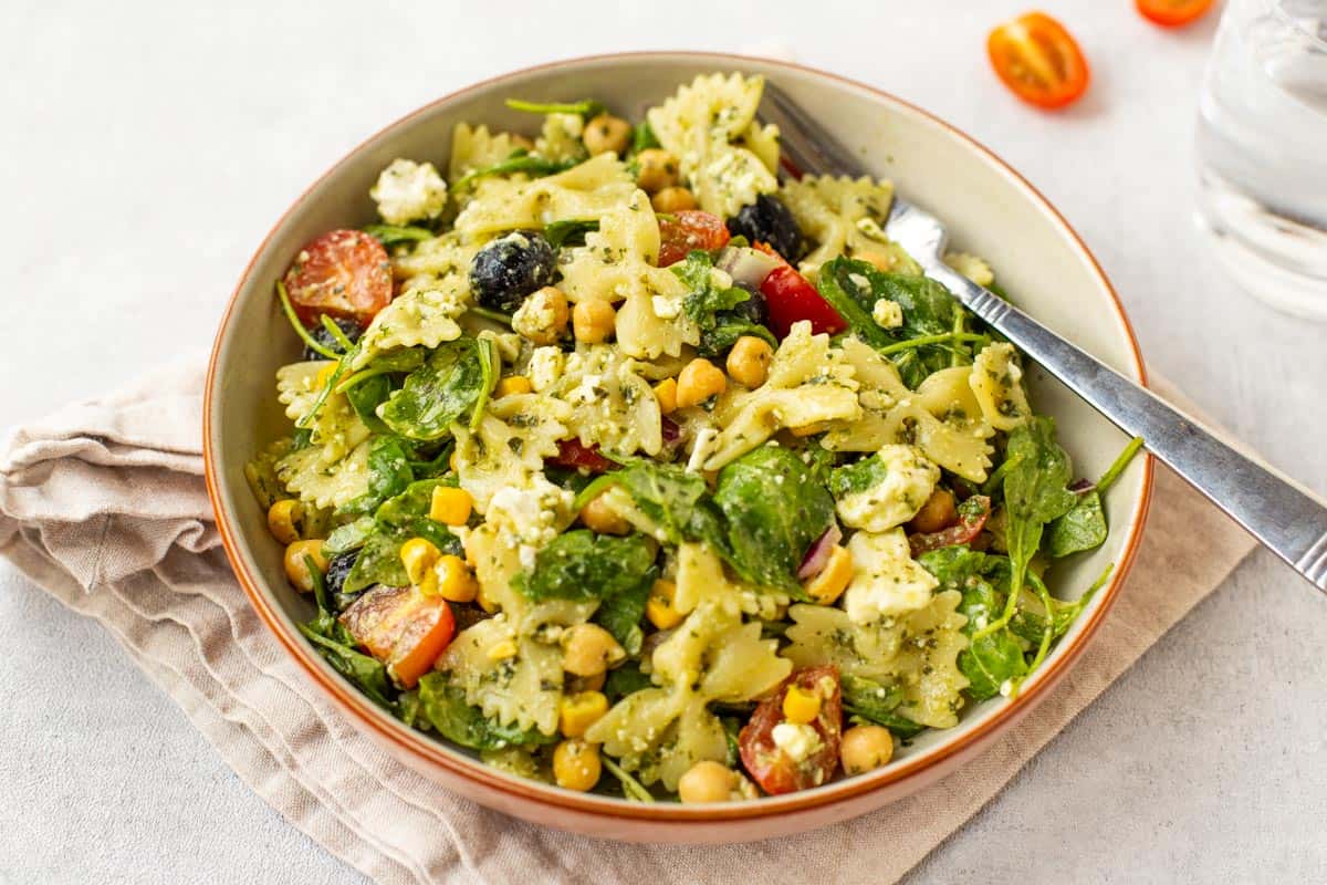 A bowlful of chickpea pasta salad with pesto and arugula.