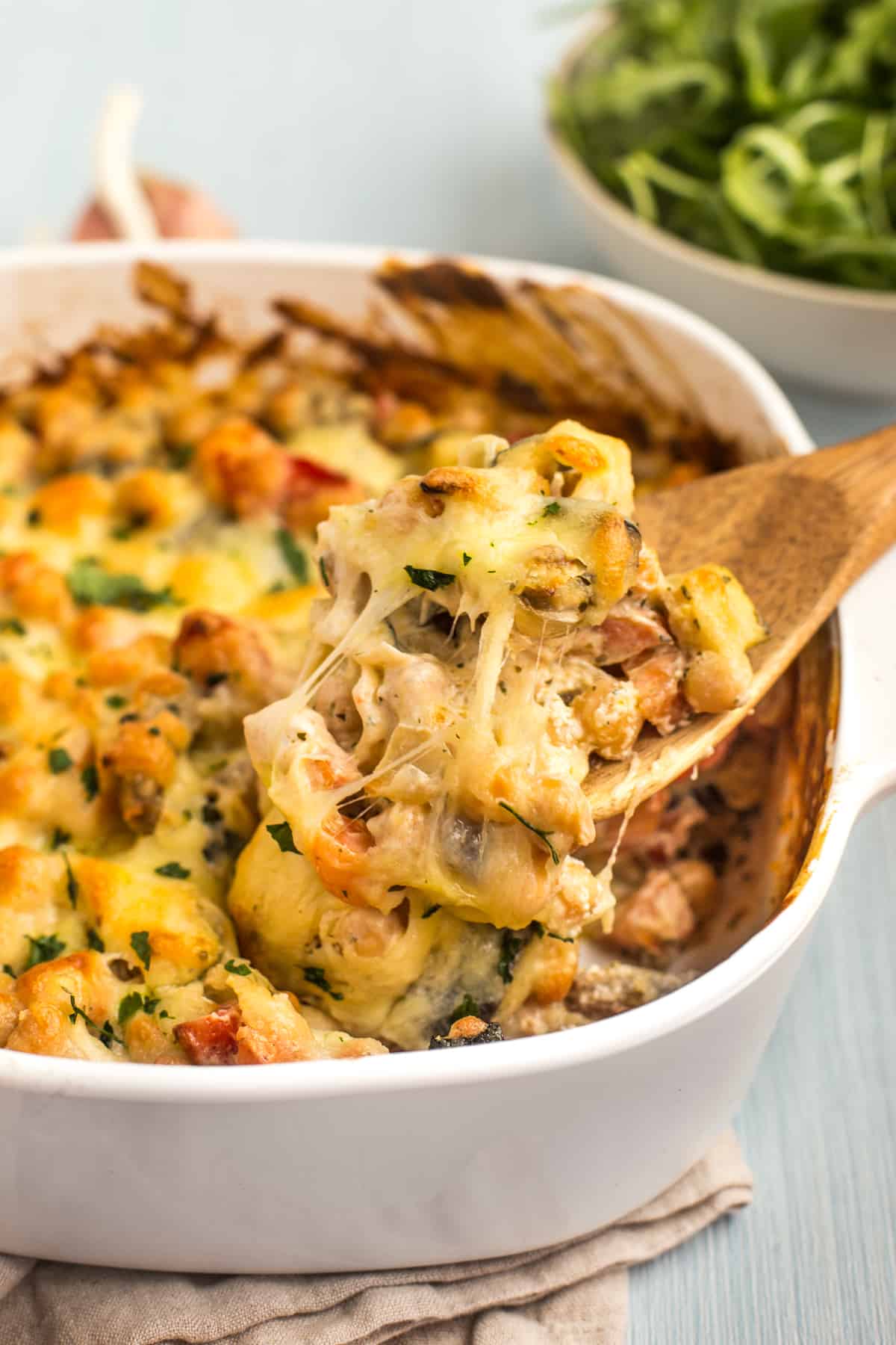 A wooden spoon taking a big scoop of creamy chickpea bake from a baking dish.