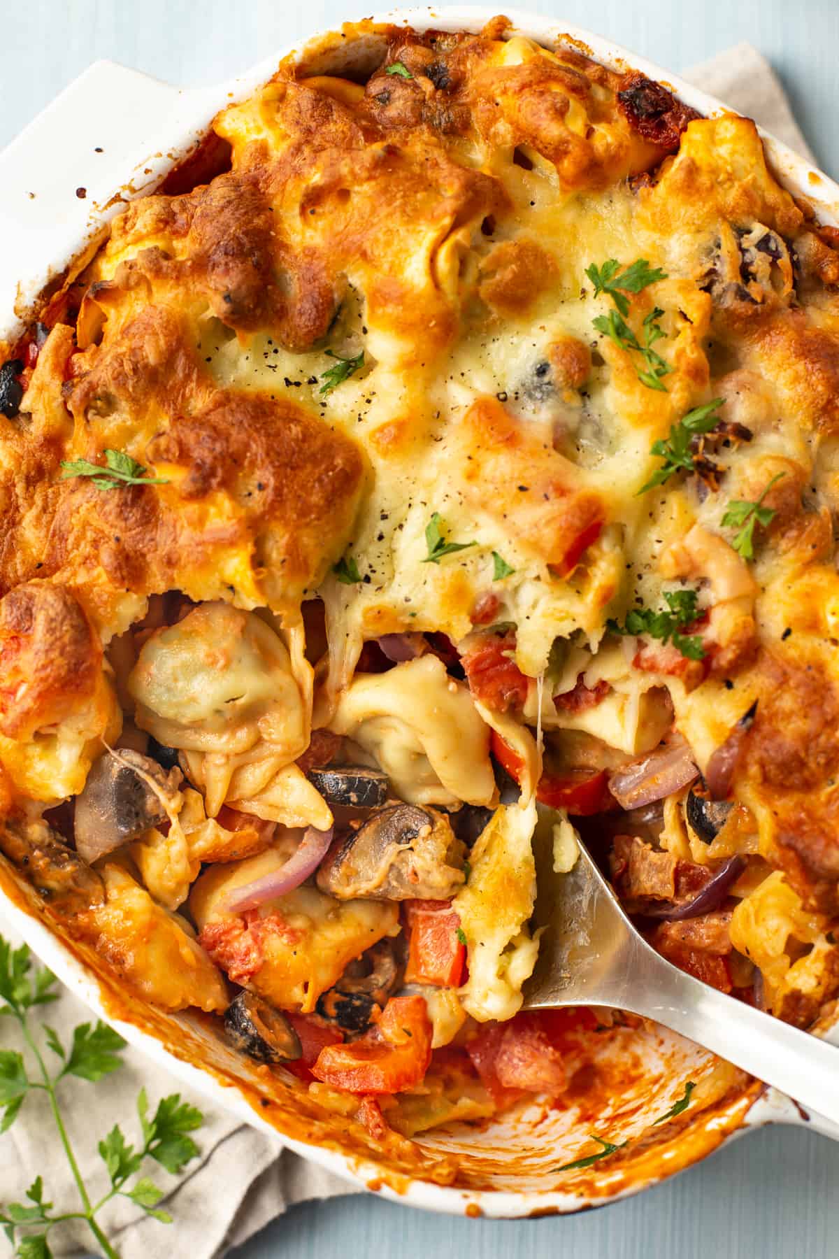 A large spoon taking a scoop of a cheesy vegetarian tortellini bake.