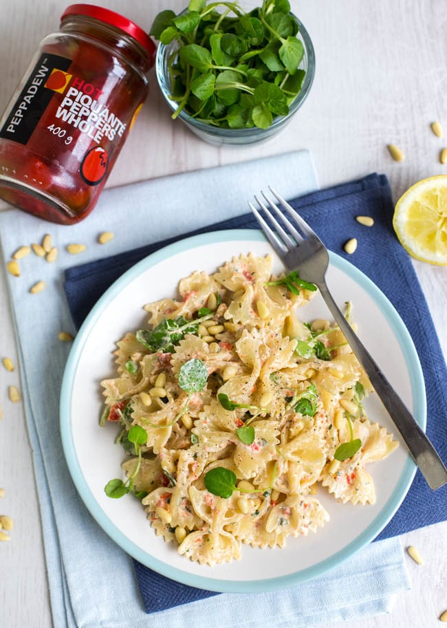 A portion of creamy farfalle pasta on a plate topped with watercress.