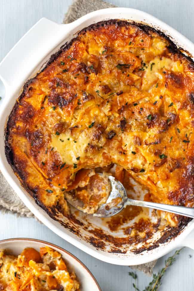 A luxurious creamy sweet potato gratin in a baking dish with a scoop removed.