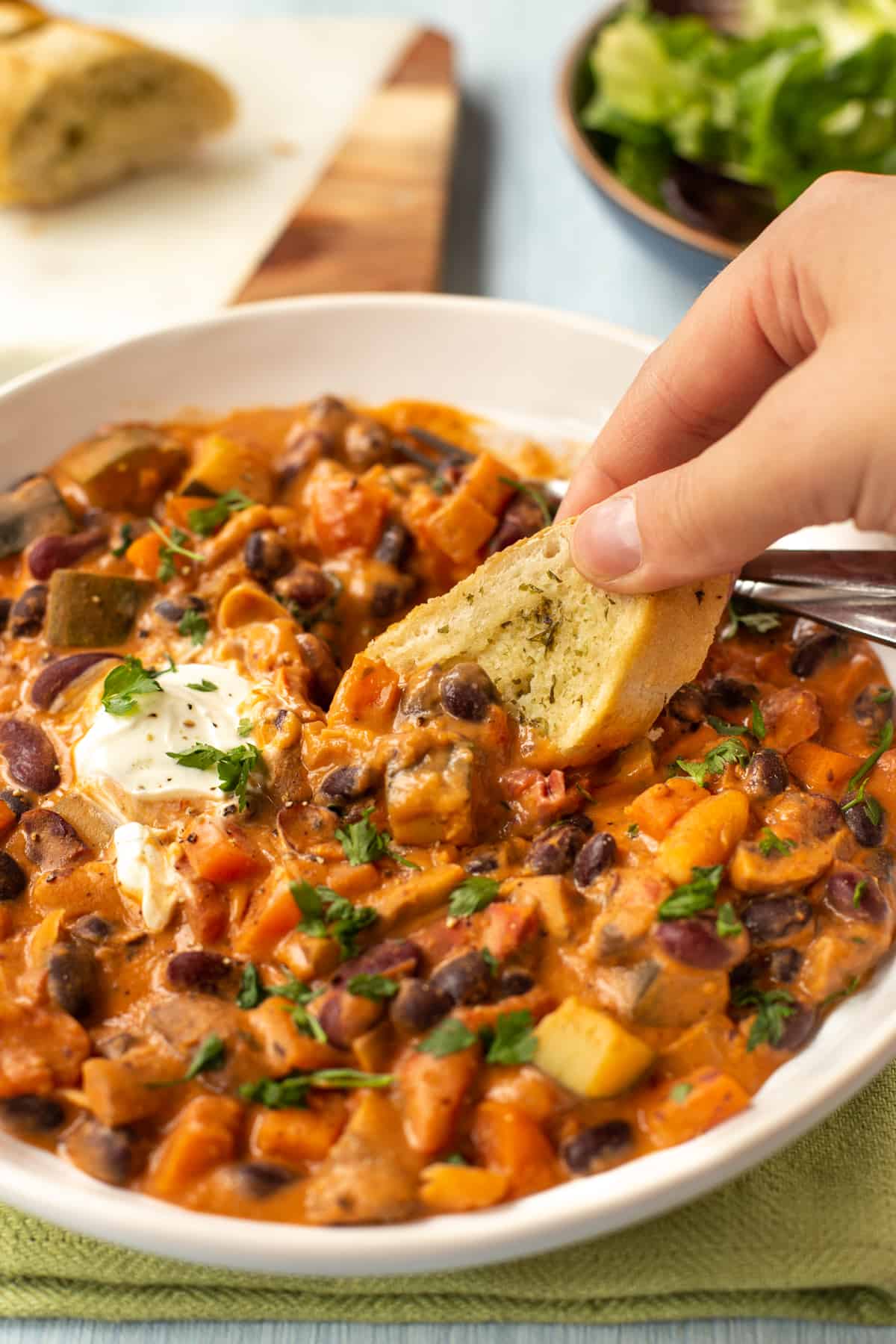 A hand using a piece of garlic bread to scoop up some three bean stew.
