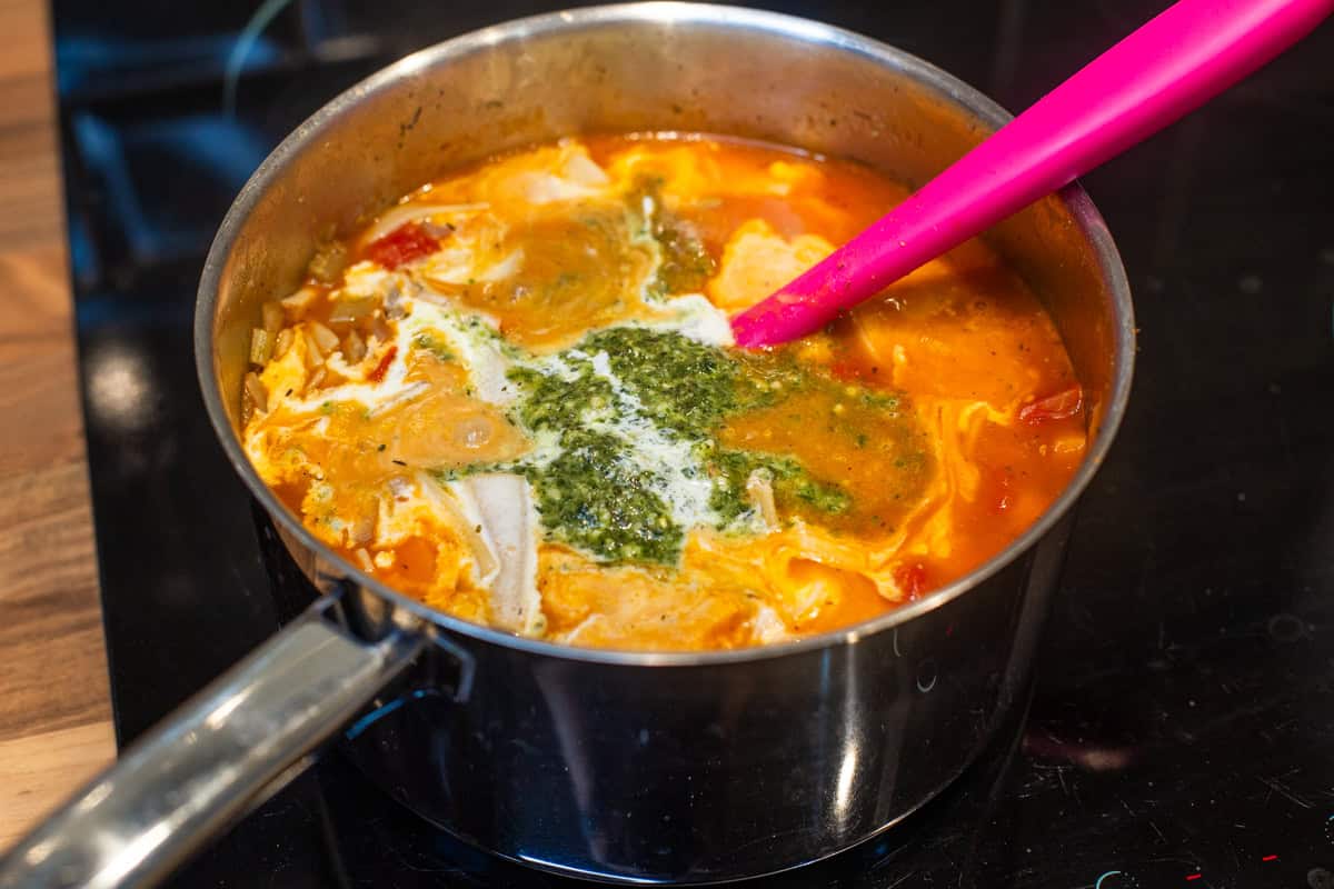 Vegetarian lasagne soup in a saucepan topped with pesto and cream.