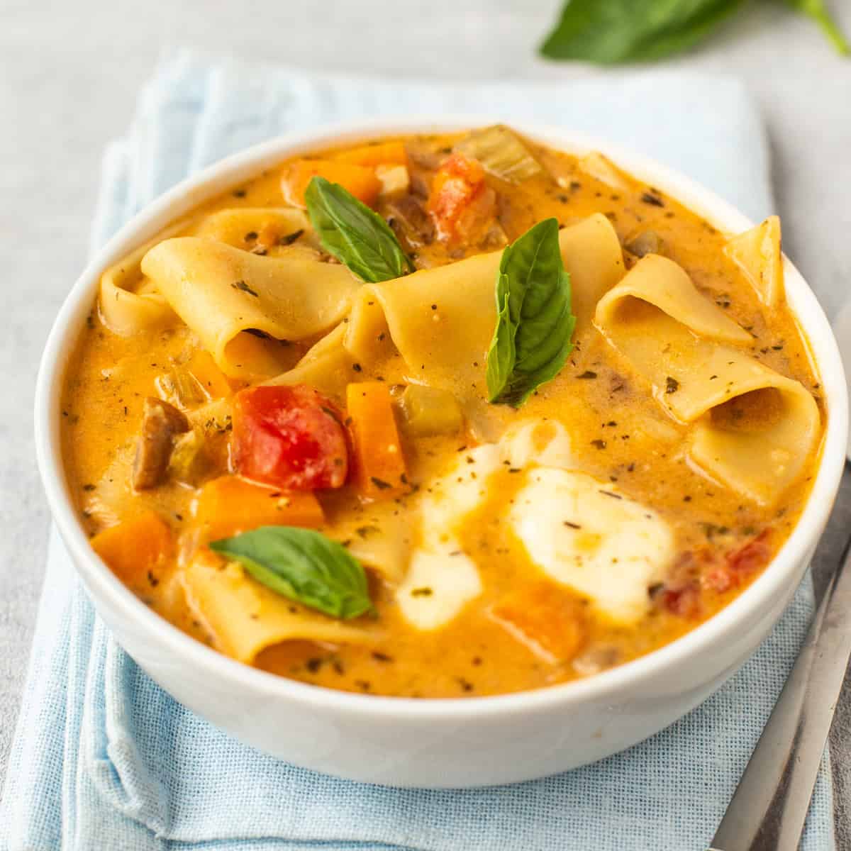 A bowl of vegetarian lasagne soup topped with fresh basil.