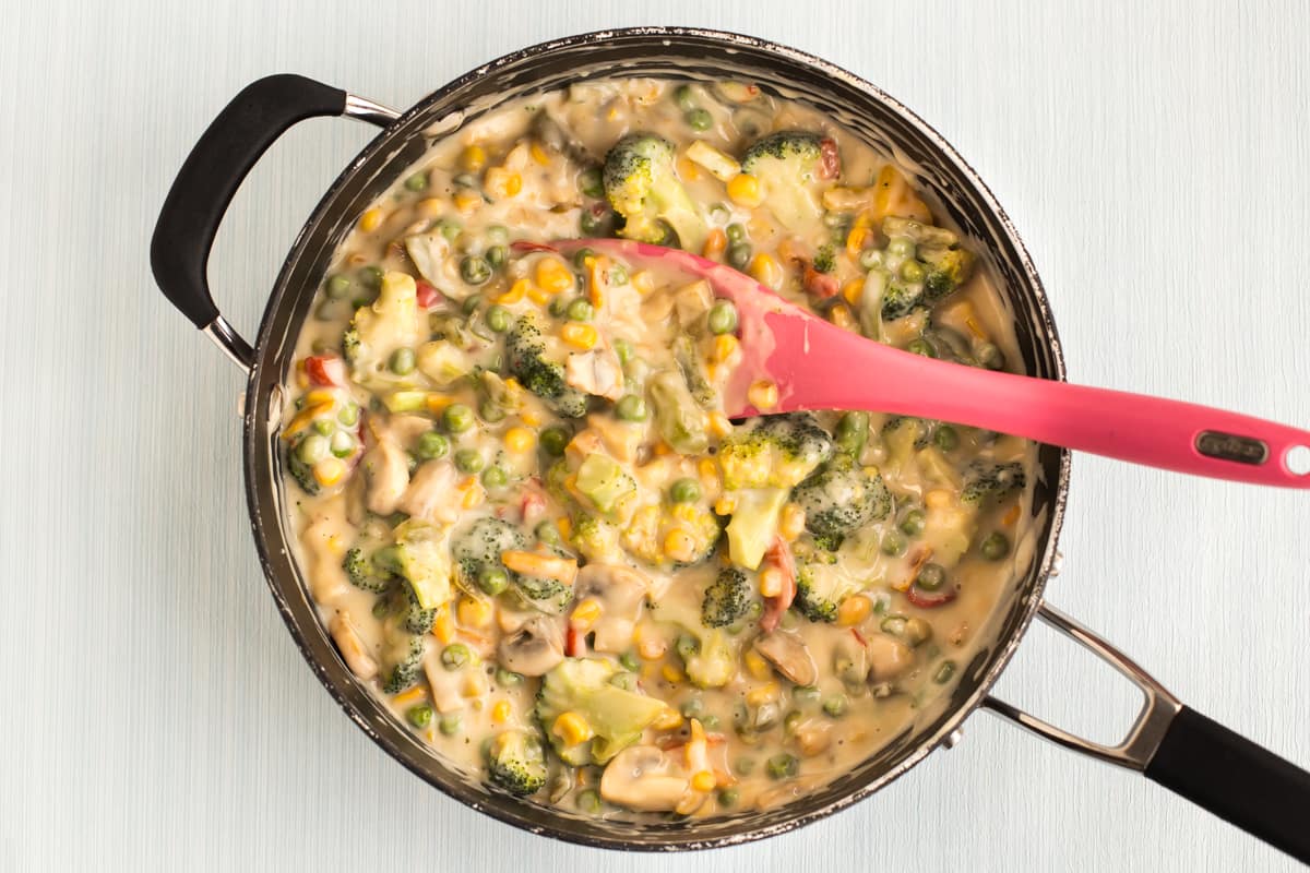 Colourful vegetables in a creamy white sauce in a frying pan.