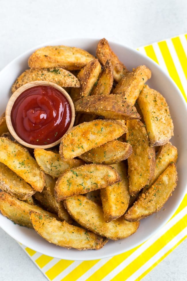 Crispy potato wedges in a bowl with a tub of ketchup and striped yellow napkins
