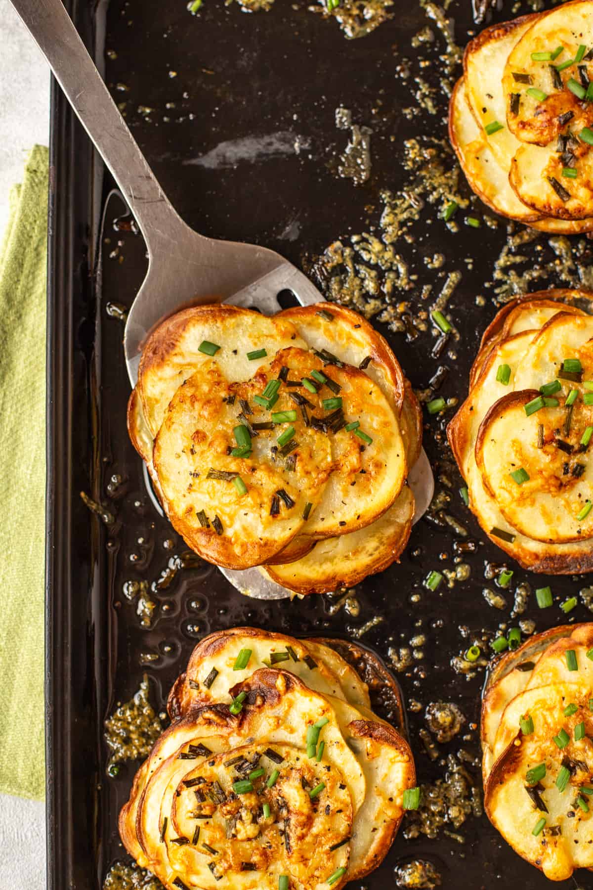 A spatula taking a stack of Easy Cheesy Potatoes Anna from a baking tray.