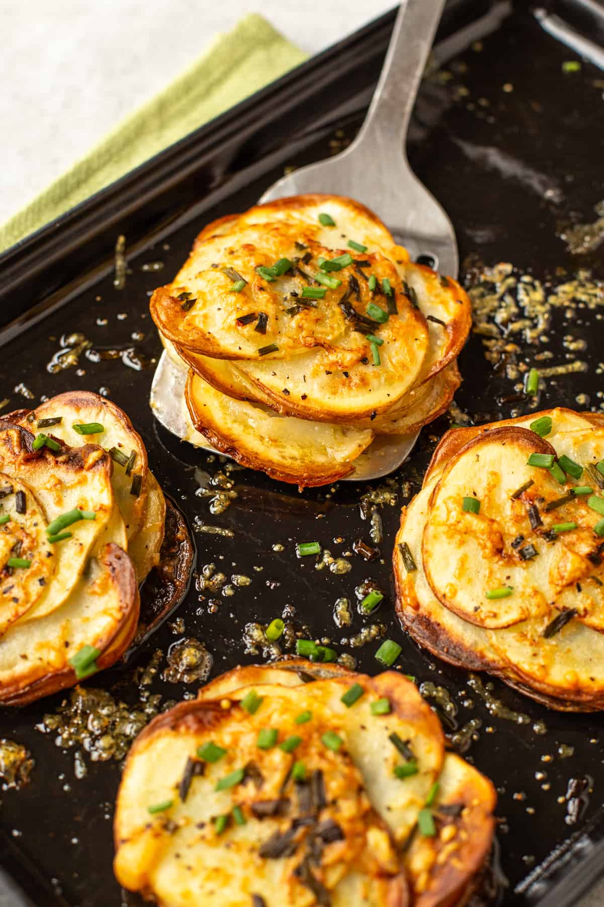 A metal spatula taking a stack of Potatoes Anna from a baking sheet.