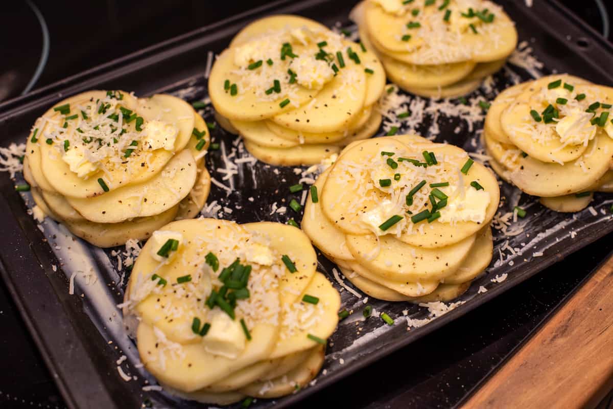 Uncooked Potatoes Anna on a baking sheet topped with butter, chives and parmesan cheese.