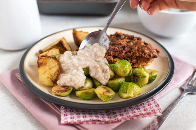 A hand spooning homemade bread sauce onto a vegetarian roast dinner.