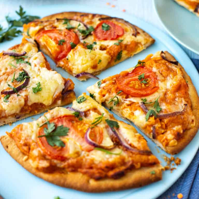 A lentil pizza topped with tomatoes and red onion, cut into quarters.