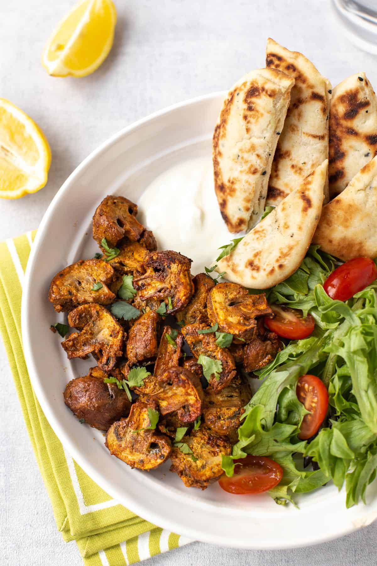 Baked mushroom tikka in a bowl with naan bread and salad.