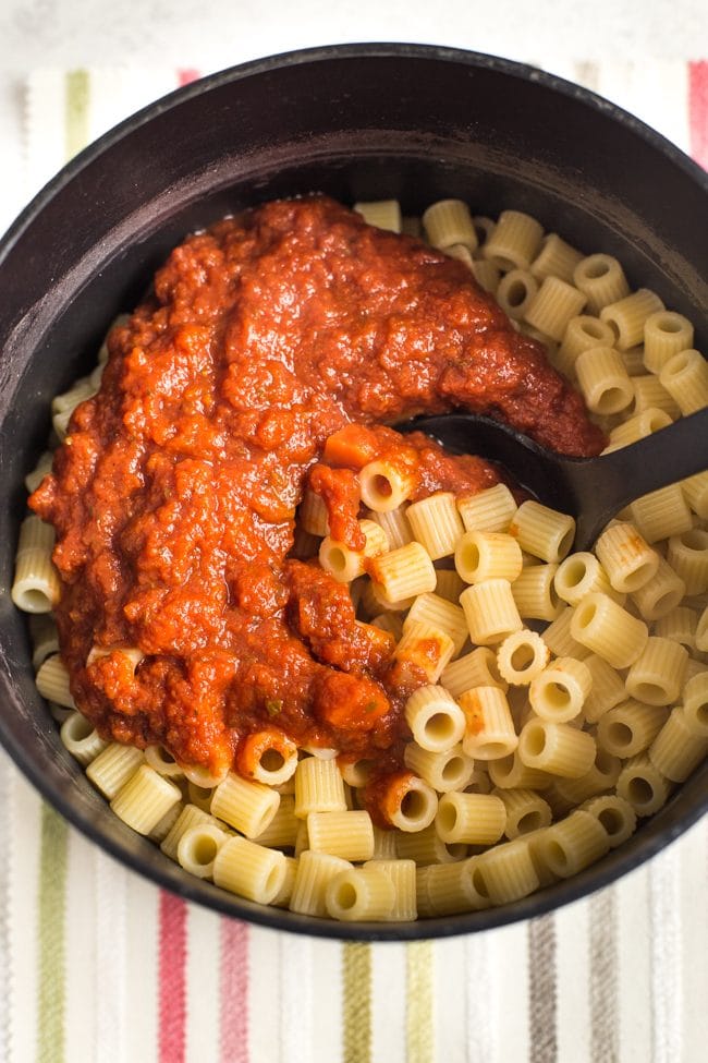 Pasta in a saucepan with tomato sauce on top