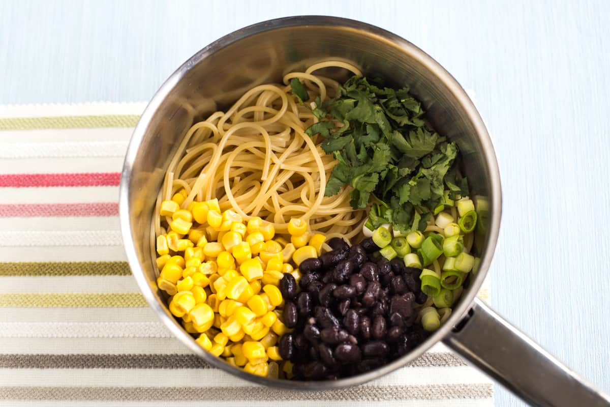 Spaghetti in a saucepan topped with sweetcorn, black beans, spring onions and cilantro