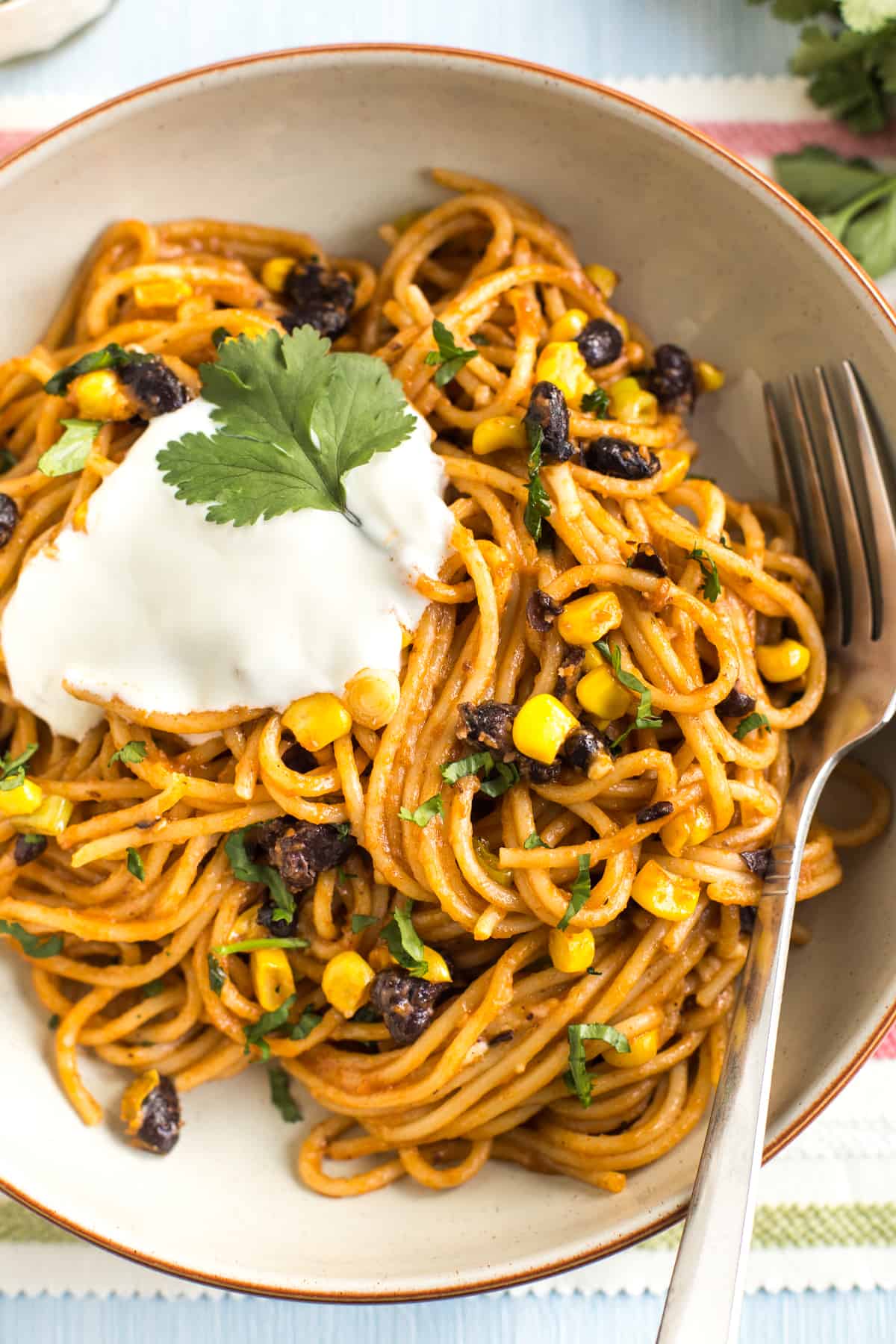 Portion of cheesy enchilada noodles in a bowl topped with sour cream and cilantro