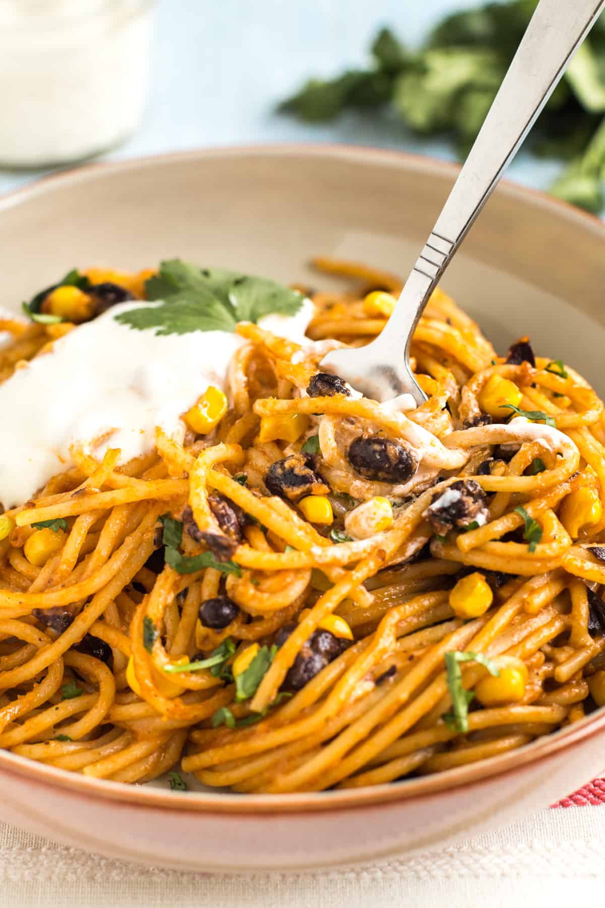 Portion of enchilada noodles topped with sour cream, being eaten with a fork