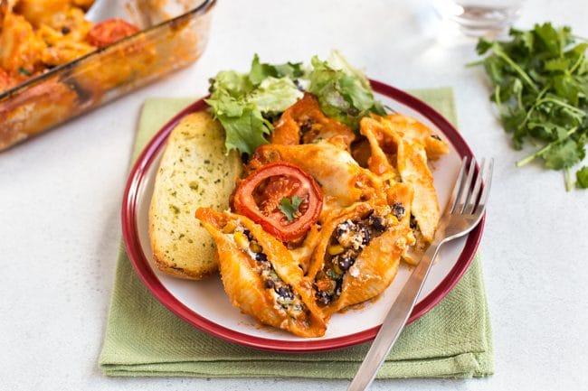 Portion of enchilada stuffed pasta shells on a plate with garlic bread and salad