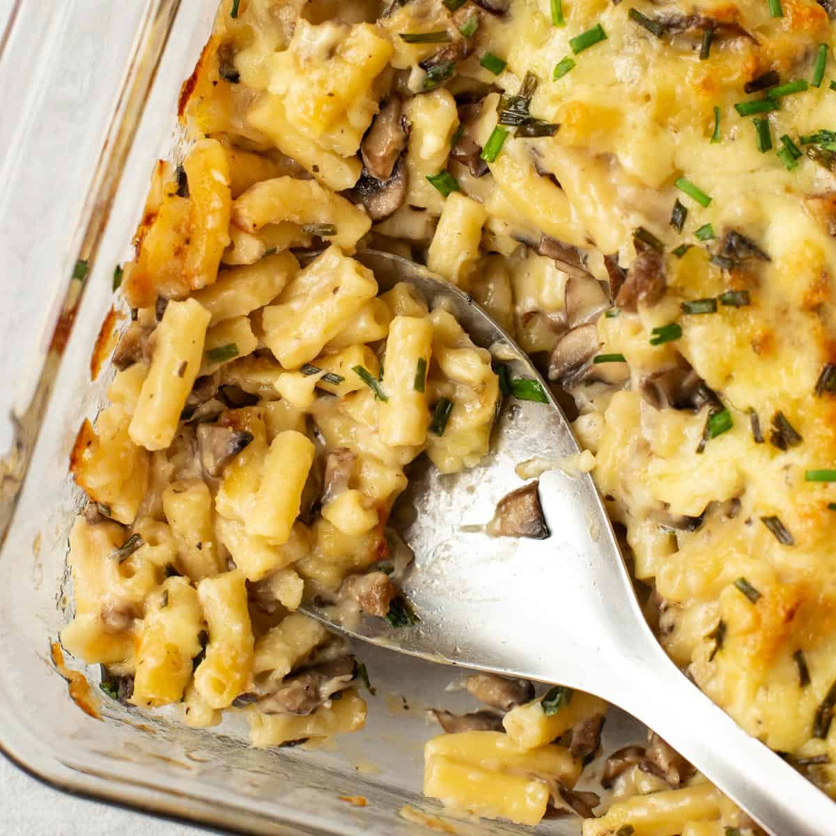 Garlic mushroom mac and cheese being scooped by a large spoon.