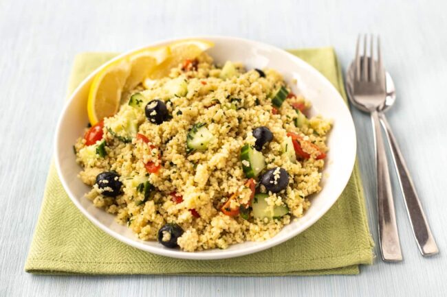 Couscous salad in a bowl with black olives and cucumbers.