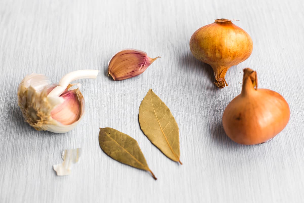 Various aromatics (garlic, bay, onion) on a table.
