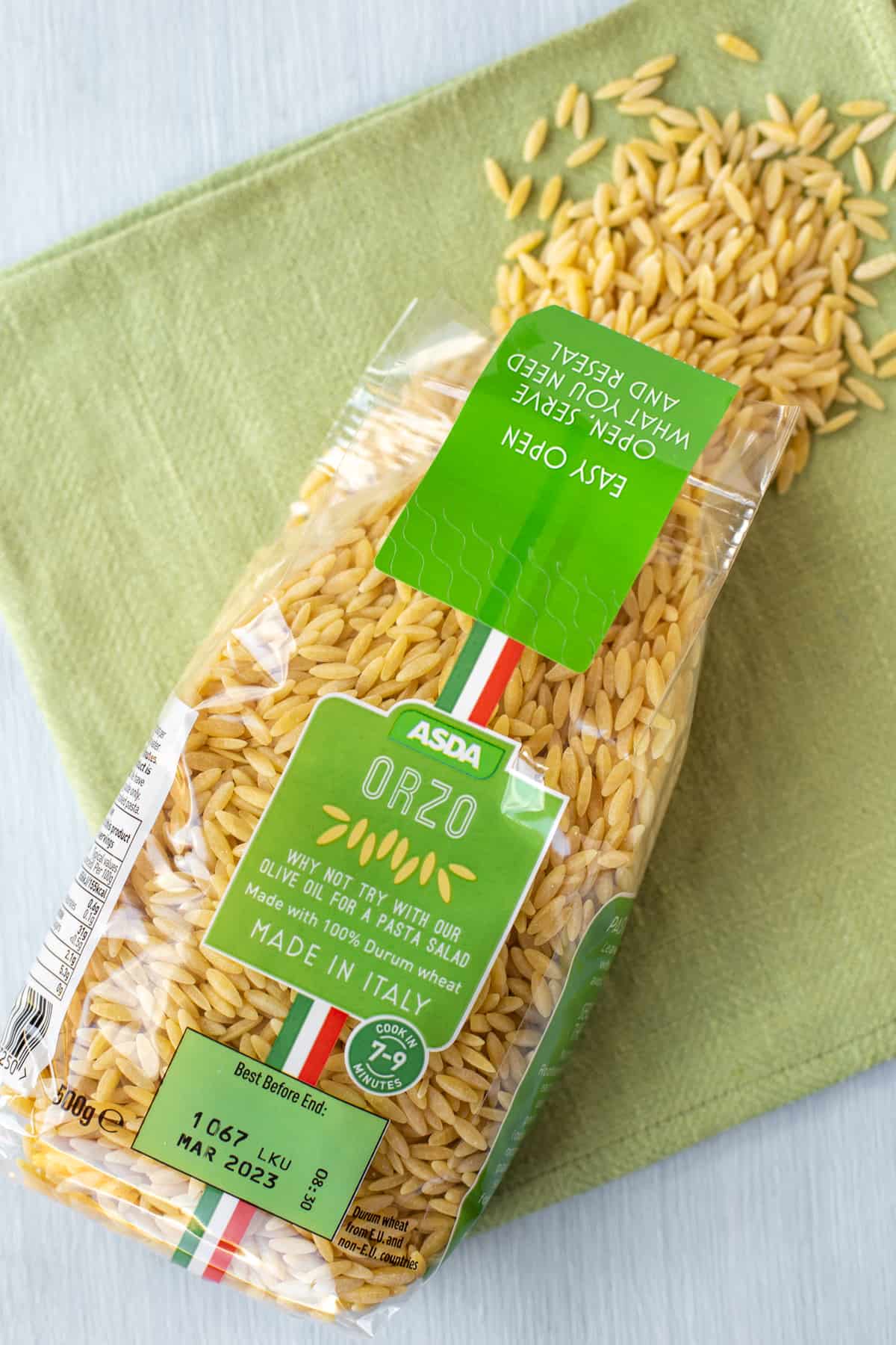 A packet of orzo spilling orzo onto a green linen.