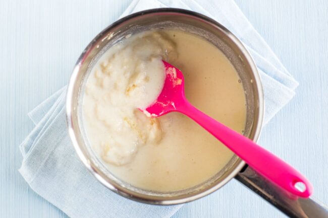 A lumpy white sauce in a saucepan - partway through cooking