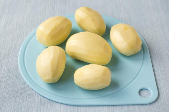 Peeled raw potatoes on a blue chopping board.