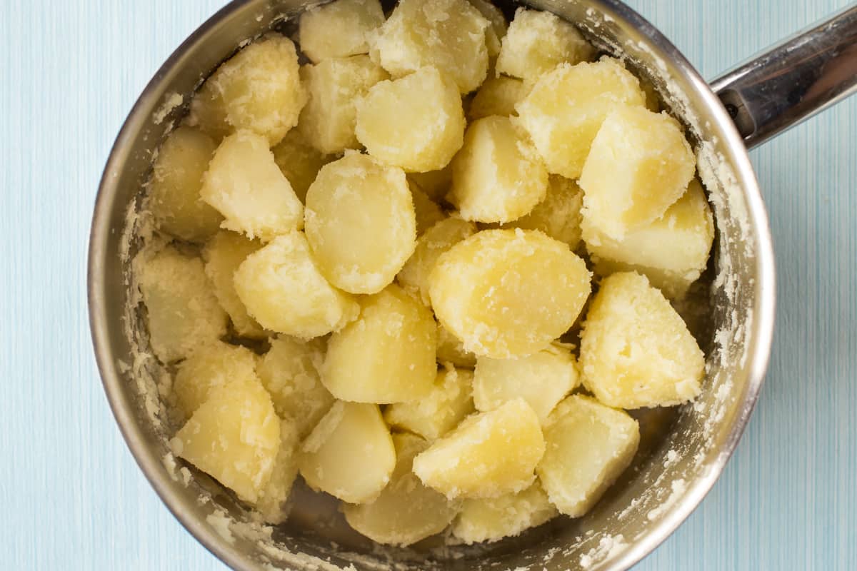 Fluffed up boiled potatoes in a large saucepan, ready for roasting.