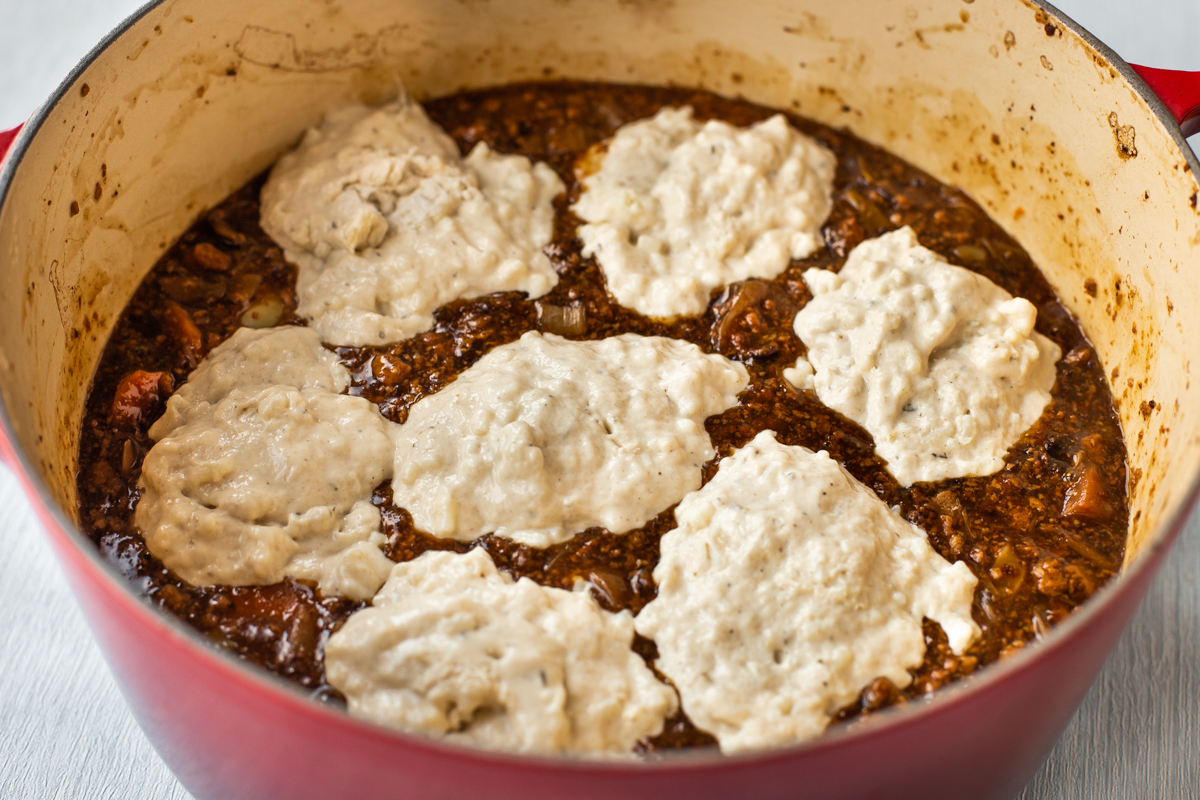 Uncooked suet dumpling mixture dolloped on top of a pot of stew.