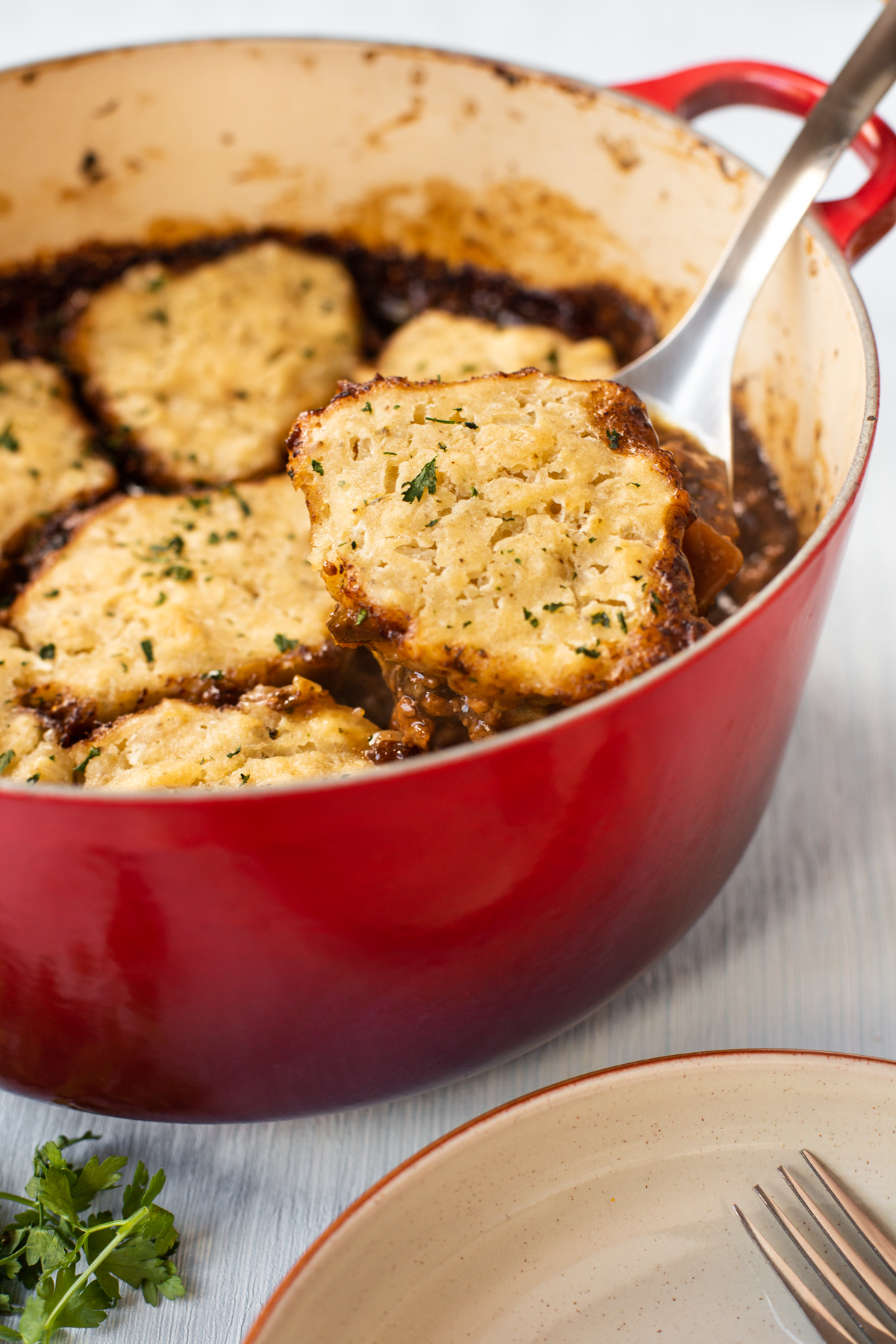 A spoon scooping a suet dumpling from the top of a casserole dish full of stew.
