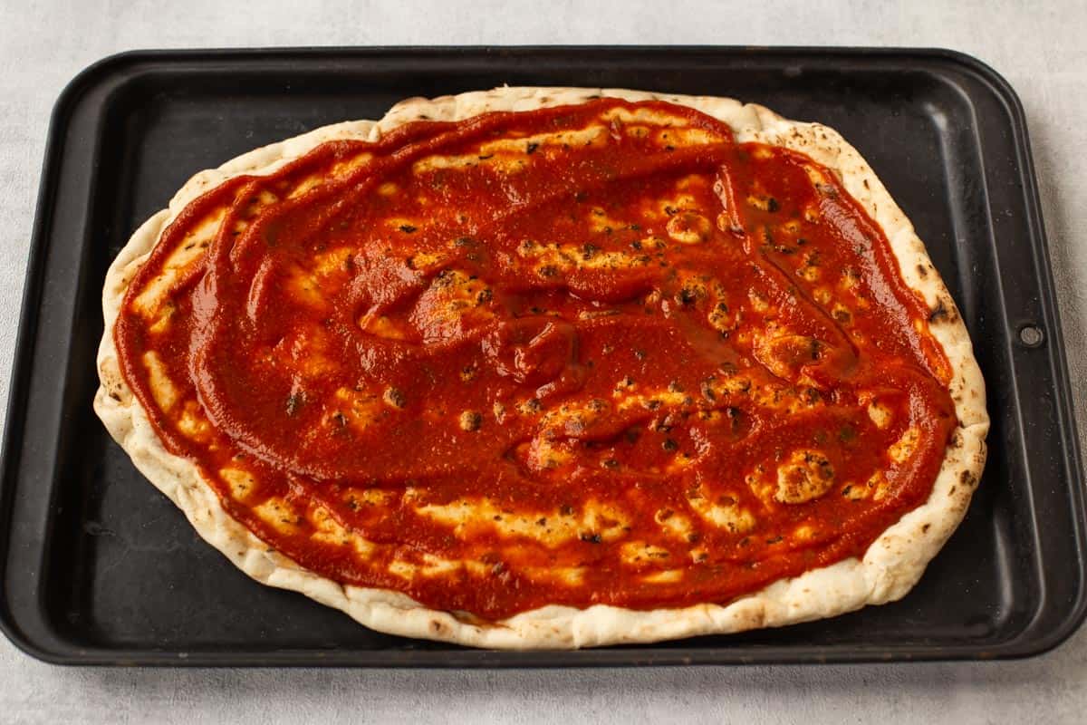 A naan bread pizza base spread with tomato sauce.