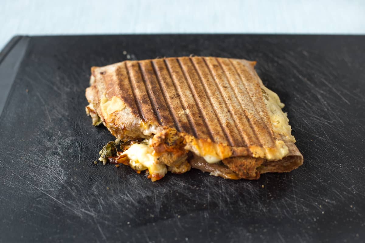 A grilled tortilla on a board with oozing cheese.
