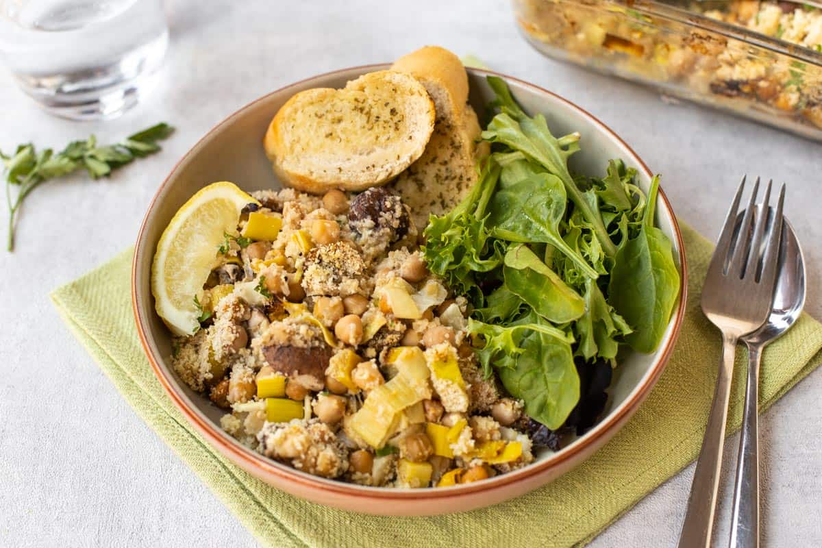 Portion of chickpea casserole in a bowl with lettuce and garlic bread.