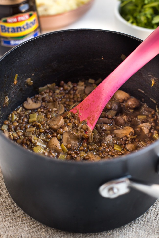 Lentil and mushroom stew in a saucepan with a jar of Branston pickle behind