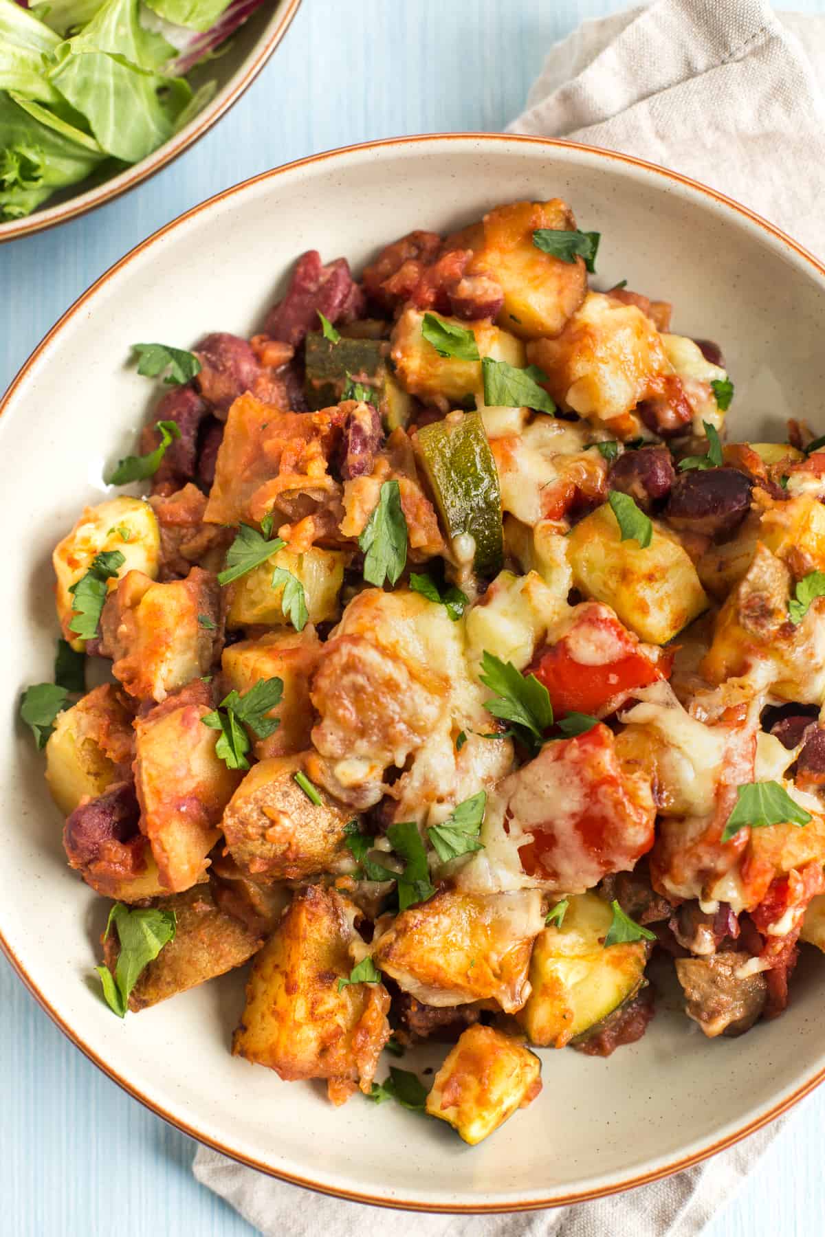 Portion of cheesy Mexican bean and potato bake in a bowl topped with cilantro.