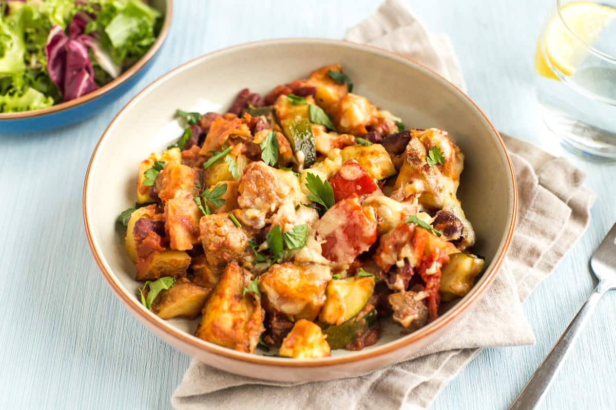 Portion of Mexican bean and potato bake in a bowl with cheese and salad.